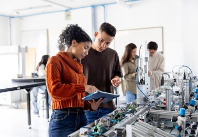 A male and female student using a digital tablet while operating a production line robot in a lab.