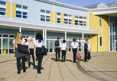 school students wearing uniform walking to school entrance carrying bags