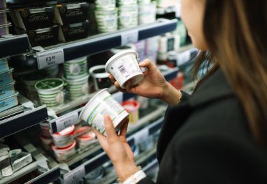 A woman in a grocery store comparing the labels on the back of two containers 