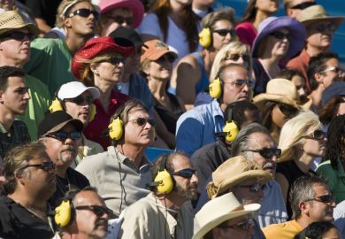 People in stadium watching car racing, listening to headphones People in stadium watching car racing, listening to headphones