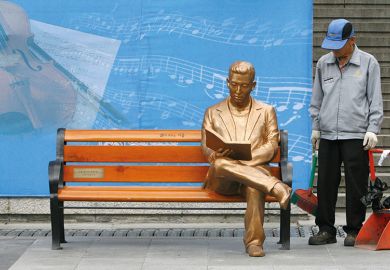 Man looks at sculpture of gold person on bench Man looks at sculpture of gold man on bench