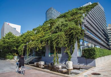 woman cycles past modern building in Japanese city with green roof of plants