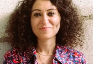 A close-up of Güllistan Yarkin, a woman with short curly hair, smiling at the camera