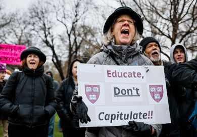 A protester holds a sign reading "Educate, Don't Capitulate!!" during a rally at Cambridge Common to urge Harvard to resist President Trump's influence on the institution, 12 April 2025.