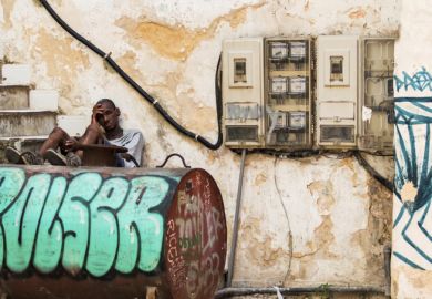 A cuban man sitting on steps with his legs on an oil tank 