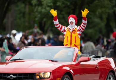 Ronald McDonald waving at spectators while going on a camaro down the road