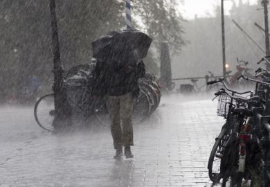 Someone with an umbrella walks through heavy rain past some bicycles