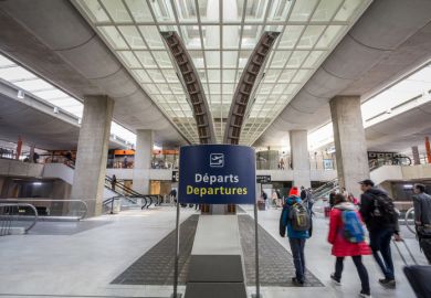 Picture of passengers with their suitcases passing near one of the displays of the departures hall of terminal 2 in charles de Gaulle Airport