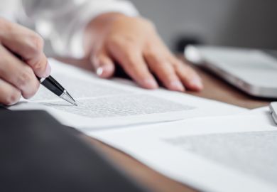 A hand clasps a pen, writing on a document