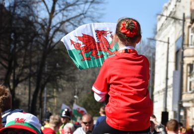 Young girl on father’s shoulders waving a Welsh flag.
