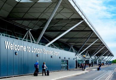 Passengers with luggage walking towards the entrance of London Stansted Airport 