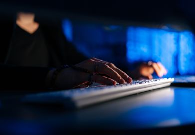 man working typing on keyboard laptop computer sitting at desk in dark room