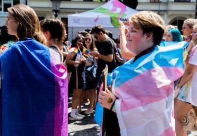A woman at a demonstration is draped in an LGBTQ flag