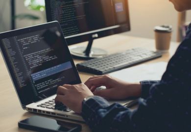 Man sits at desk, typing into a laptop