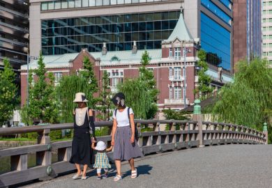 Two Japanese women lead child over bridge into Kokyo Gaien National Garden.