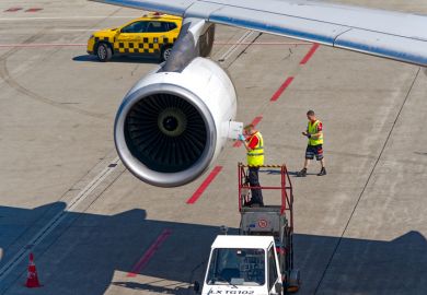 Airport technician doing maintenance work at jet engine of Edelweiss Air Airbus A340-300 HB-JMC airplane on a sunny summer day.