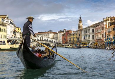 View of the beautiful Rialto Bridge spanning the Grand Canal with gondolier in foreground in Venice, Italy