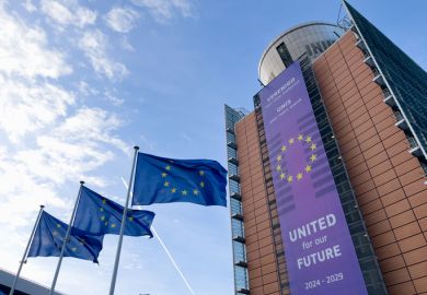 Several EU flags and the exterior view of the European Commission headquarters in Brussels,