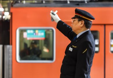 Unidentified Japanese train conductor gives a hand sign to a train while making a stop at Osaka Station.