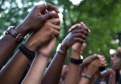 Interlocked hands at a Black Lives Matter protest. BAME academics are facing dual pandemics of Covid and racism.