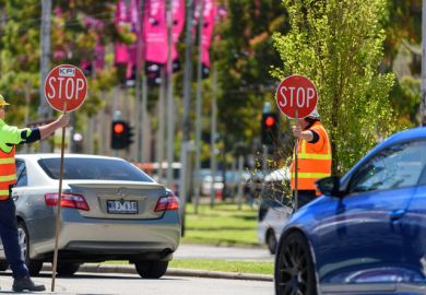 Two traffic control workers are holding stop signs to stop the traffic at a roundabou Two traffic control workers are holding stop signs to stop the traffic at a roundabout
