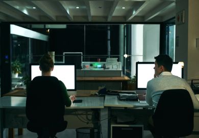 Rearview shot of two businesspeople working on computers in an office at night