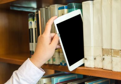 Hand placing a tablet on a library bookshelf