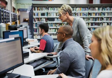 Librarian helping student at computer in library Librarian helping student at computer in library