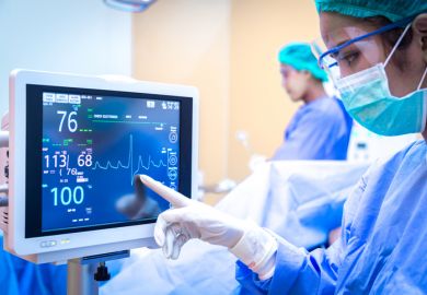 A surgeon watches as a line on a monitor spikes downwards, symbolising cuts to health research