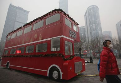 A man wearing mask passes a London double-decker bus model during a heavy pollution day in Beijing, China. Illustrating transnational education (TNE).