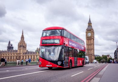 London, UK - July 8, 2015 Double-decker and the Big Ben in London. The bus is driving across the Westminster bridge with people walking in the background.