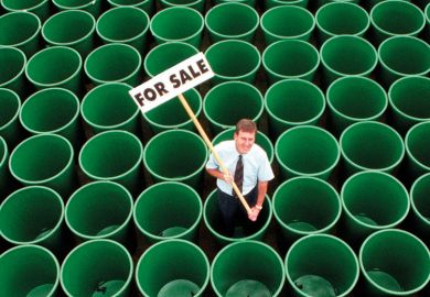 Man standing in rows of green plastic water butts, holding 'For sale' sign
