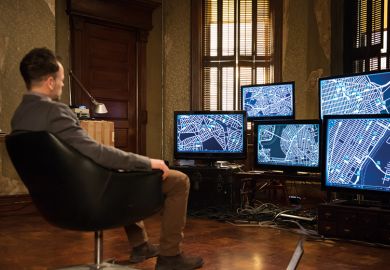 A man sitting in front of a bank of computer screens A man sitting in front of a bank of computer screens