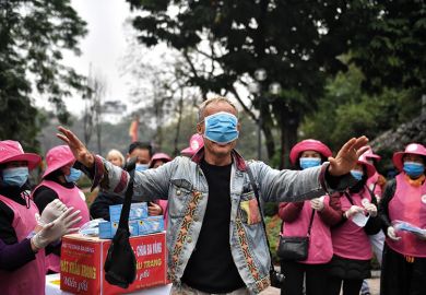 Man with medical mask over eyes surrounded by a crowd of people