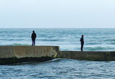 Men standing in opposite directions on seafront wall