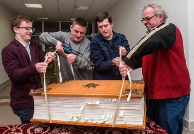 Men struggling to lift a giant book. To illustrate that three major research universities have opted out of new Elsevier deal amid concerns over the cost. Men struggling to lift a giant book. To illustrate that three major research universities have opted out of new Elsevier deal amid concerns over the cost.