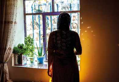 Iranian Kurdish woman who was circumcised at eight stands in silhouette by a window
