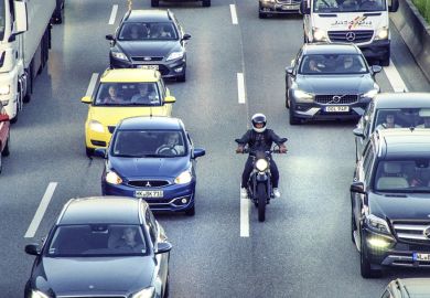 A motorbike slips through a traffic jam, symbolising rapid completion of a PhD