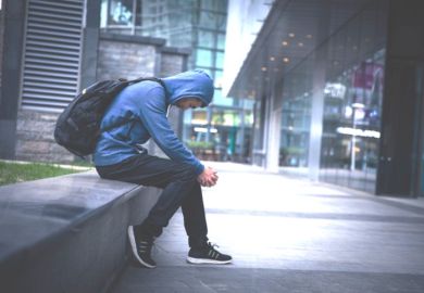 A young man in a hoodie sitting on a city street, illustrating NEETs A young man in a hoodie sitting on a city street, illustrating NEETs