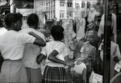 New York City, NYS, USA, 1951. Afro-American teenagers in front of a shop window in Harlem. They look at the offers of a fashion store.