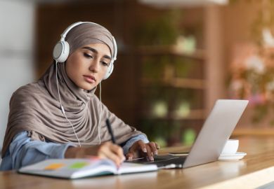 A woman in headscarf participating in an online lesson in a cafe