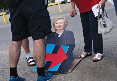 People looking at cardboard cutout of Hillary Clinton lying on road
