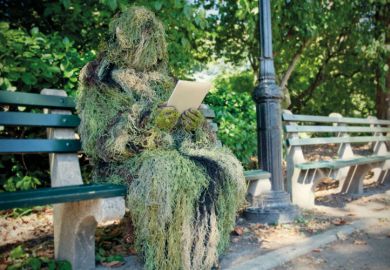 Person in ghillie suit reading on bench
