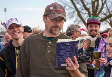 A man reads a Donald Trump book while waiting in a long line for admission to a Trump campaign rally, 2016. To illustrate that academics might need to 'tread carefully' with courses on Trump. A man reads a Donald Trump book while waiting in a long line for admission to a Trump campaign rally, 2016. To illustrate that academics might need to 'tread carefully' with courses on Trump.