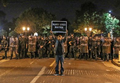 A man holds a placard saying ‘Black Lives Matter’ before a line of policemen