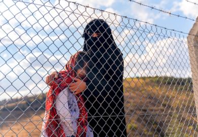 A refugee mother and her child behind a migrant camp fence