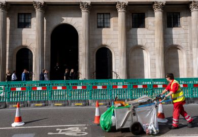 A street cleaner walks past a barrier in front of a columned building, as an illustration of how working-class people can feel excluded in higher education