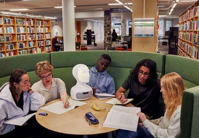 Students in a library with a robot head on the table. To illustrate AI risk to university jobs.
