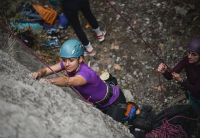 One rock climber hold the rope for another, illustrating a supportive research environment