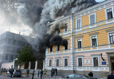 Heavy smoke billows out of a historic yellow and white building as a man tries to escape out of a window on the third floor